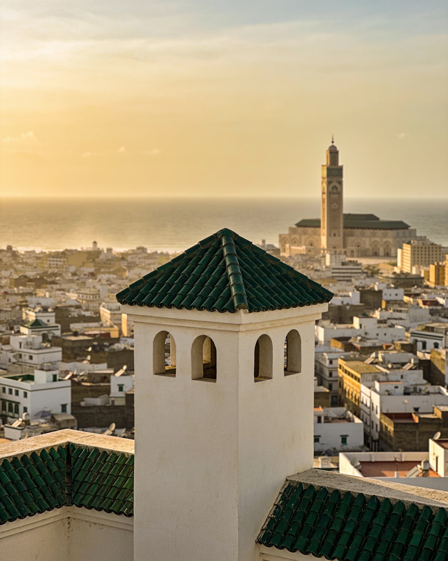Toits de Casablanca au coucher du soleil, tuiles vertes au premier plan et minaret de la mosquée Hassan II au fond, face à l'Atlantique
